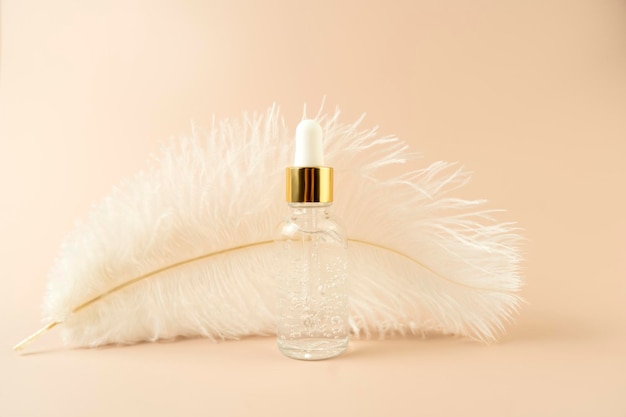 A white feather and a face serum or natural oil standing on a beige background
