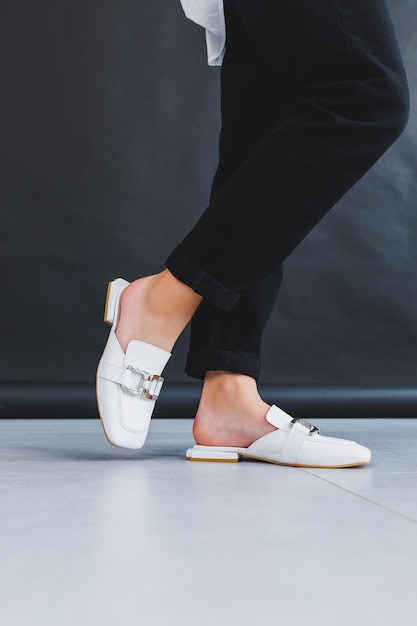 여성의 다리에 흰색 여성 가죽 슬리퍼 근접 촬영 여성의 여름 가죽 신발의 새로운 컬렉션