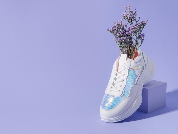 Photo white female sneakers with sequins with flowers inside on purple background with geometric cube podium