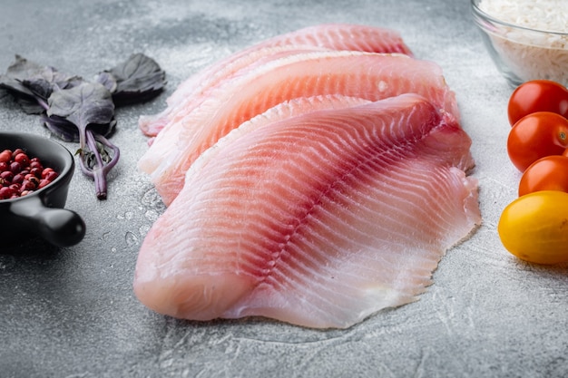 White fish fillet, with basmati rice and cherry tomatoes ingredients, on gray table