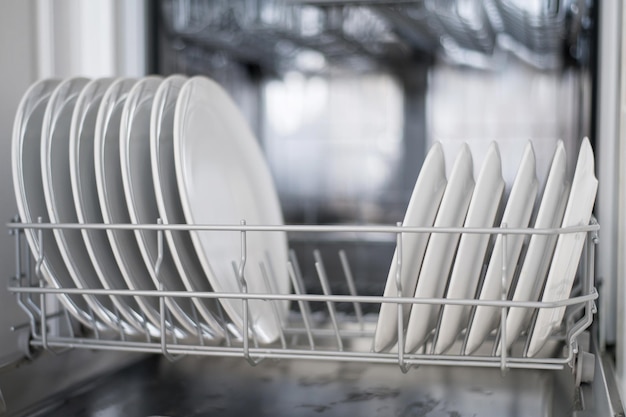 Белые плоские тарелки, большие и маленькие, загружаются в посудомоечную машину.