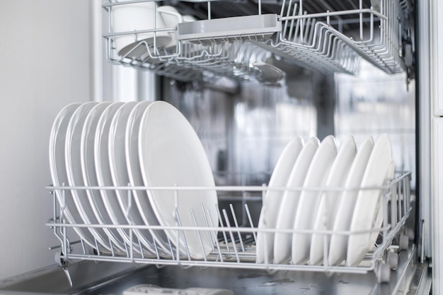 Белые плоские тарелки, большие и маленькие, загружаются в посудомоечную машину.