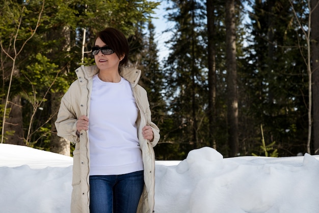 冬の森で非対称の髪型の女性をフィーチャーした白いフリースのクルーネックのスウェットシャツのモックアップ。ヘビー級スウェットシャツテンプレート