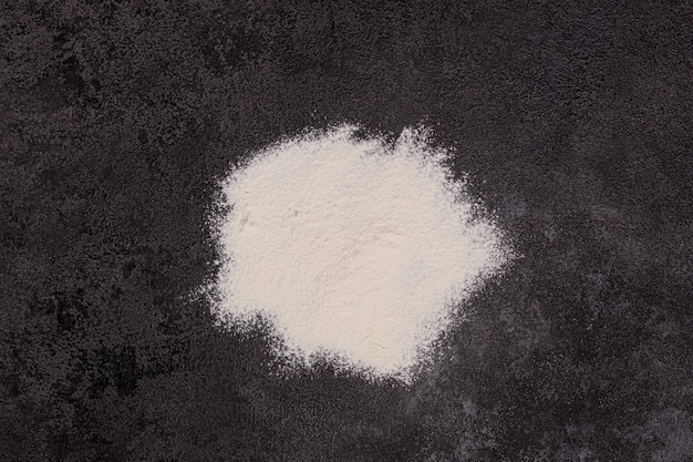 White flour on a black structural background. The beginning of cooking. Process. Bakery products