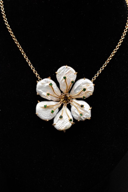 A white flower necklace with green stones and green diamonds.