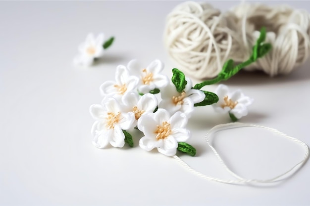 A white flower with green leaves sits next to a ball of yarn.