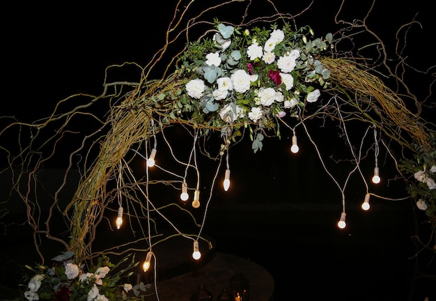 White flowers arch at the wedding ceremony Outdoors decoration Romantic rustic style Lamps lights in the evening