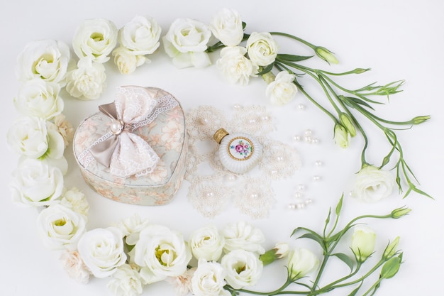 White flowers lined with a heart-shaped jewelry box, perfume bottle, pearls and lace