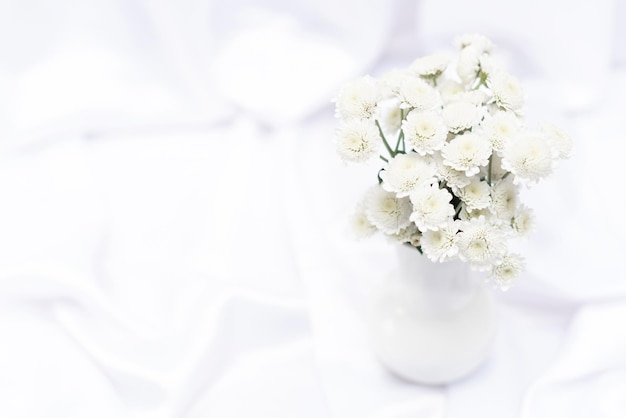 White flowers in white vase on white background with copy space and selective focus Greeting or invitation card