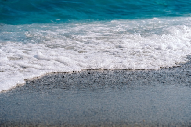 White foamy waves on sandy beach closeup. Seaside on sunny summer day.