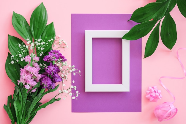 White frame and bouquet flowers on pink purple wall.