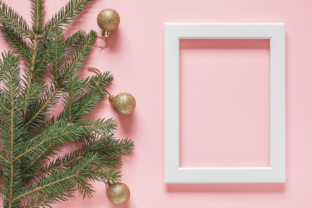 White frame and green spruce branch with gold christmas balls on pink