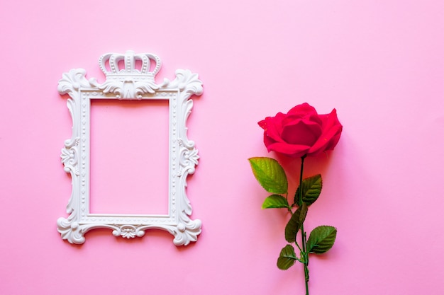 A white frame and hearts over pink background and a bouquet of red roses