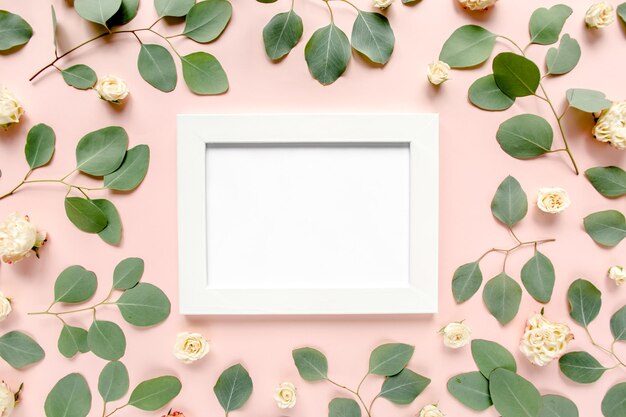 Photo white frame is decorated with green eucalyptus leaves roses floral pattern on a pink background the apartment lay top view floral frame