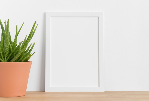 White frame mockup with a aloe vera in a ceramic pot on a wooden table Portrait orientation