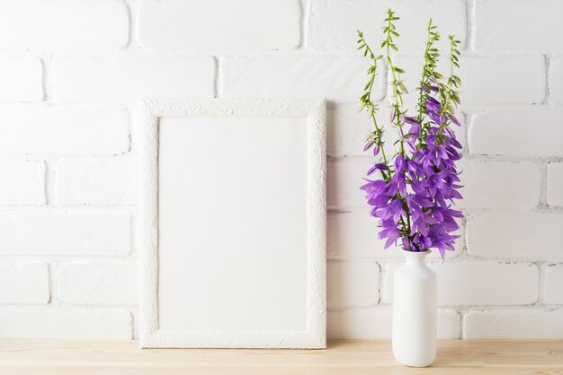 Mockup di cornice bianca con bouquet di campanula viola vicino al muro di mattoni