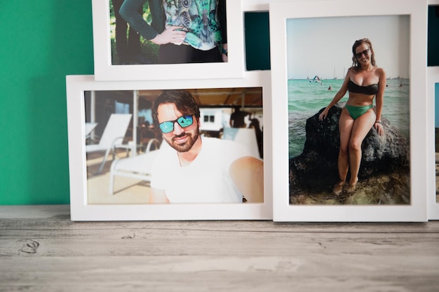 A white frame of several photos of a couple, with a gray wooden background and a blue-green fabric.