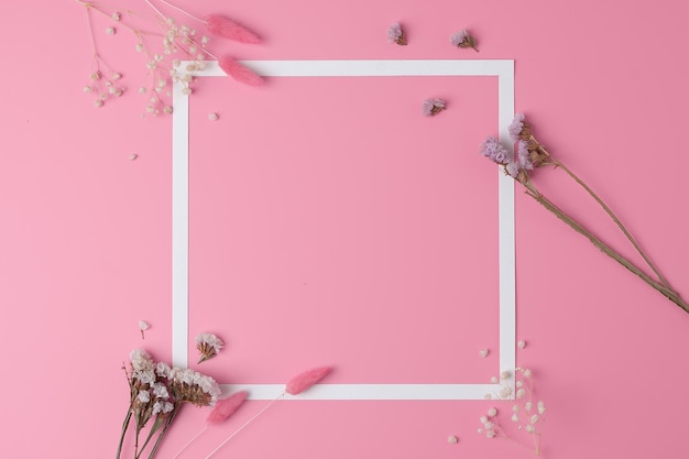 Photo white frame with flowers on pink background flat lay copy space