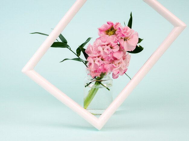 white frame with flowers in styled vase near blue wall.