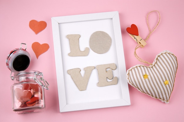 Foto cornice bianca con lettere amore, cuore rosso e vaso con cuori su uno sfondo rosa pastello