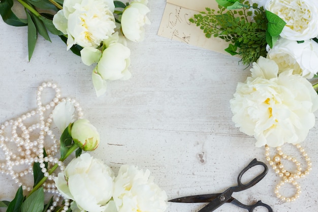 White fresh peony flowers with pearls jewellery on white wooden desktop frame