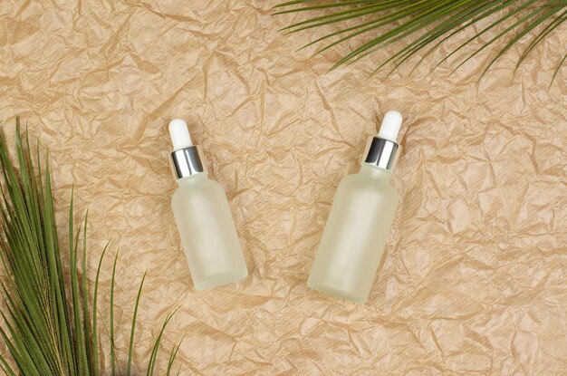 White frosted bottles with essential oils on a crumpled beige paper background Cosmetic bottles with face serum