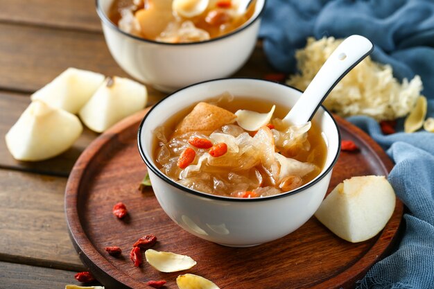 Foto zuppa di funghi bianchi e pera in ciotola bianca su piatto di legno