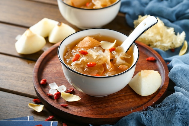 Foto zuppa di funghi bianchi e pera in ciotola bianca su piatto di legno