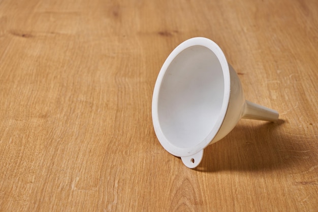 A white funnel is laying on a wooden floor.