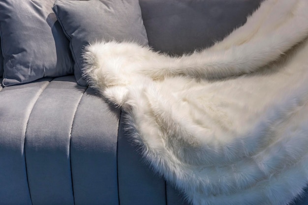 White fur fluffy plaid on a gray velor sofa Coziness and comfort in interior decoration Closeup Space for text