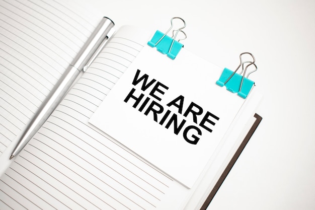 white future calculator, paper sheet, pink paper clips and silver colored pen. text we are hiring