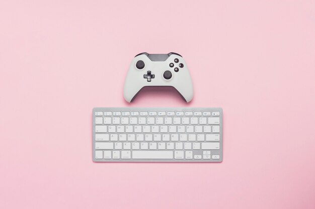 White gamepad and keyboard on a pink background. Tactics of the game. Concept game on the console and PC, computer games. Flat lay, top view.