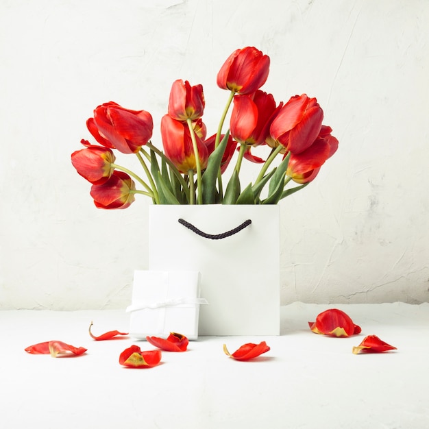 White Gift bag, small white gift box and bouquet of red tulips on a light stone. Concept Offers an engagement or marriage