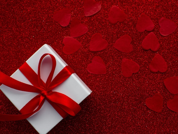 Белая подарочная коробка находится на фоне бумаги с красным сердцем, вид сверху