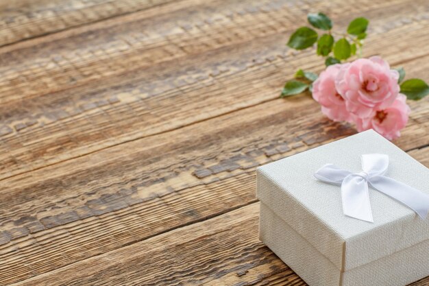 ピンクのバラで飾られた古い木の板に白いギフトボックス。コピースペースのある上面図。