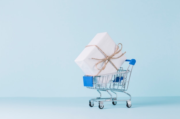 White gift box in shopping cart on blue backdrop