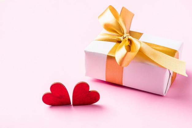 Белая подарочная коробка с золотой бантовой лентой и деревянной поздравительной открыткой с красными сердечками