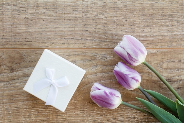 White gift box with beautiful tulips on the wooden boards Concept of giving a gift on holidays