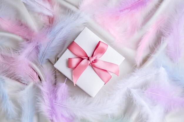 사진 색 실크 텍스처 배경에 분홍색 리본을 가진 색 선물 상자 다채로운 새 털 휴가
