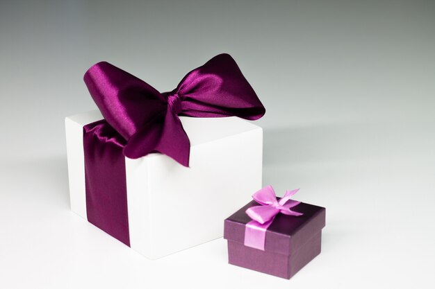 Confezione regalo bianca con nastro viola e presente viola, su sfondo grigio