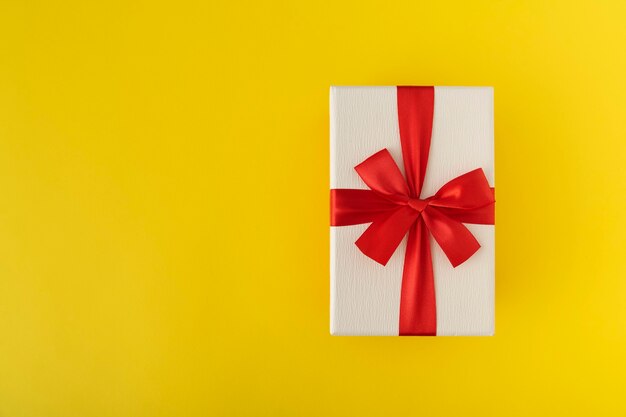 White gift box with red bow on yellow background. Copy space.