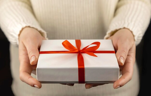 White gift box with red ribbon in beautiful female hands holiday concept