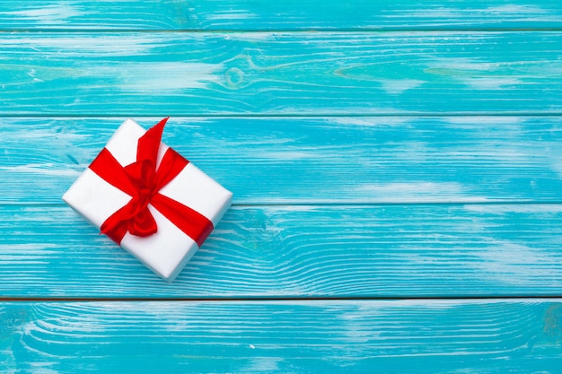 White gift box with red ribbon on blue wooden background, top view