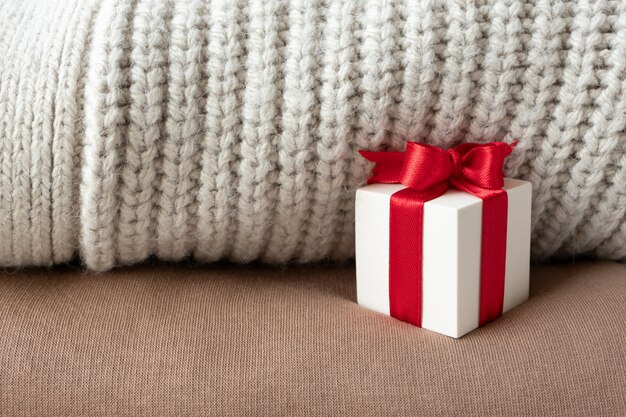 White gift box with red ribbon bow on beige warm knitted sweaters