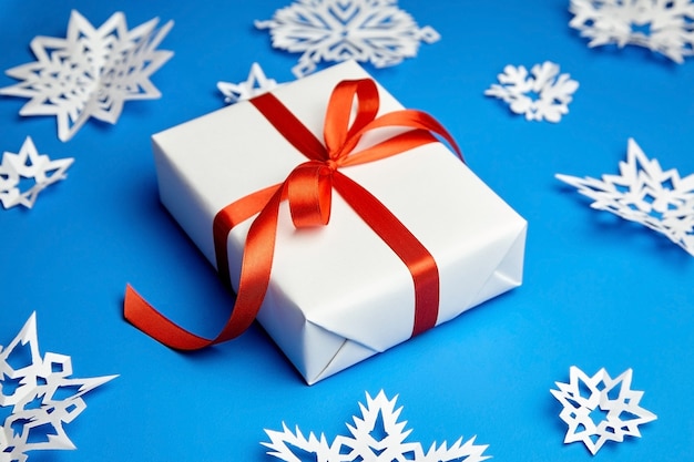 White gift box with red ribbon and paper snowflakes on blue