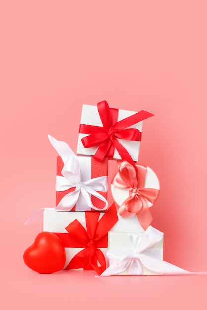 White gift boxes with red satin ribbons on a pink background. Festive presents for St. Valentine's Day, International Women's Day, wedding or engagement.