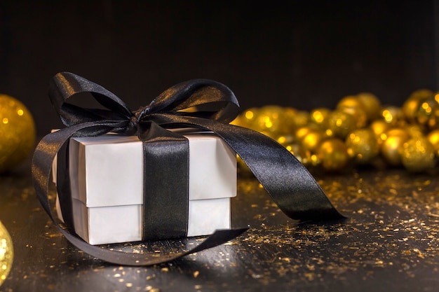 White gift with a black ribbon on a black table with golden toys.