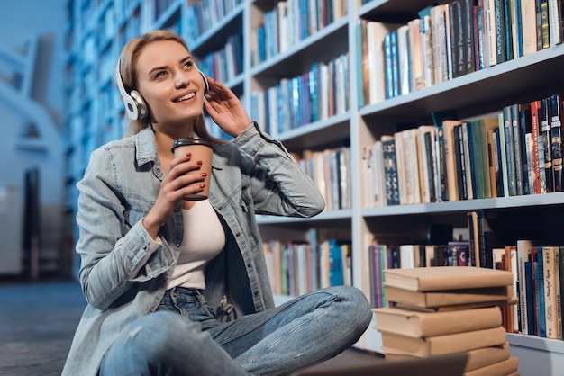 White girl near bookshelf in library. Student is listening to music.