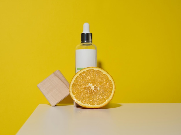 White glass bottle with a pipette and half an orange on a white surface, green background. Citrus extract