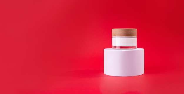 White glass jar of cream on a stand white podium on red background Design Template of Fashion